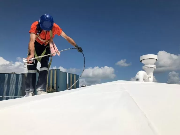 image of a person applying mascoat protective coating with a jet spray to a roof to prevent corrosion and vapour loss.